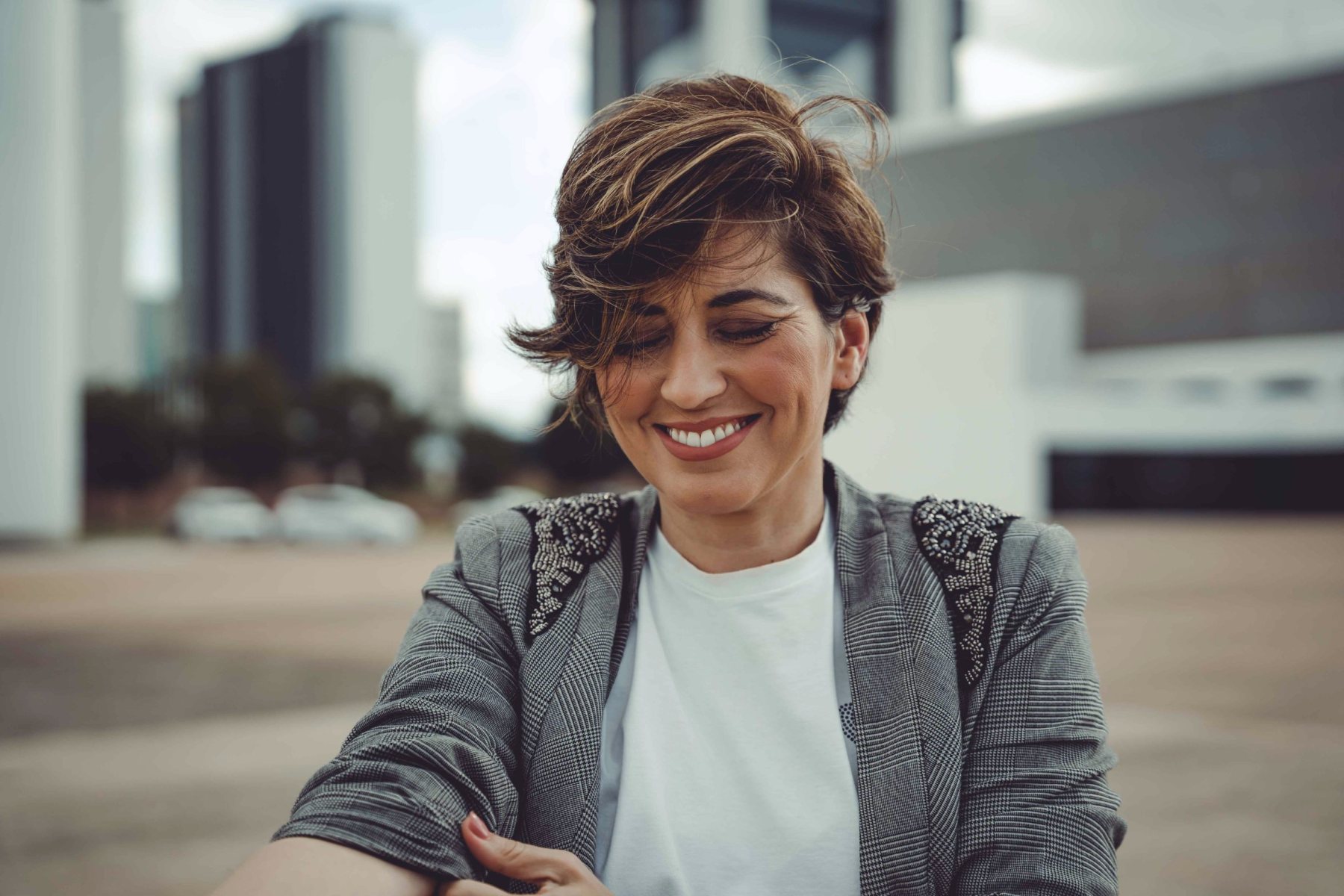 Alline sorrindo e olhando para baixo enquanto ajusta a manga do blazer
